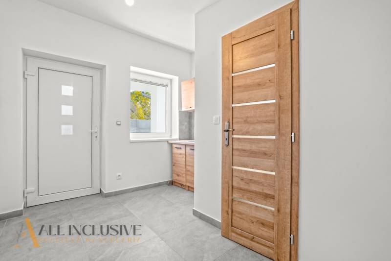 Weißer Flur eines Einfamilienhauses mit Holztüren und Keramikboden.