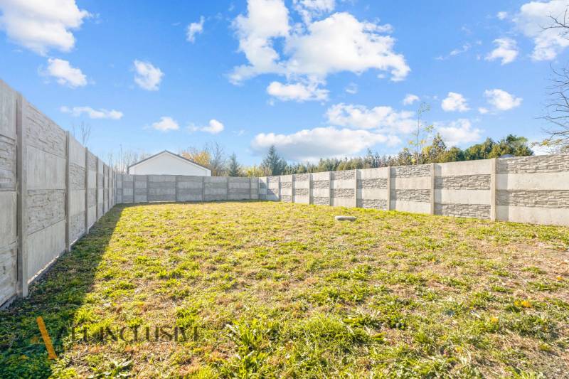 Der Garten eines Einfamilienhauses in Orechová Potôň mit einer Betonmauer und einer Rasenfläche.