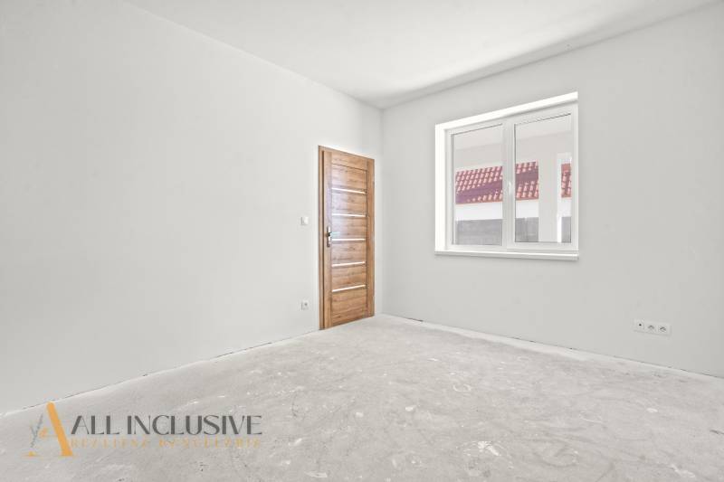 Ein Einfamilienhaus mit einer weißen Wand und einer Holztür, ein Fenster mit Blick auf das Dach.