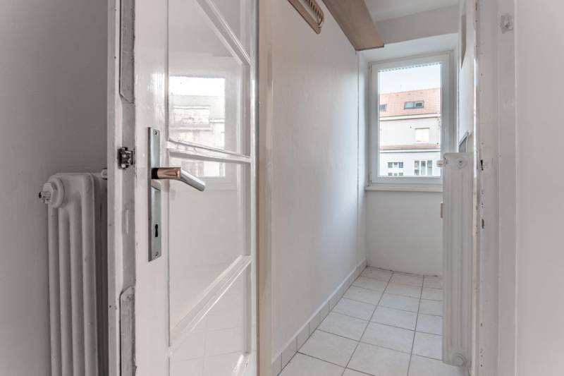 Ein schmaler Raum mit einem Fenster, Fliesenboden und einem weißen Heizkörper in einer 3-Zimmer-Wohnung.