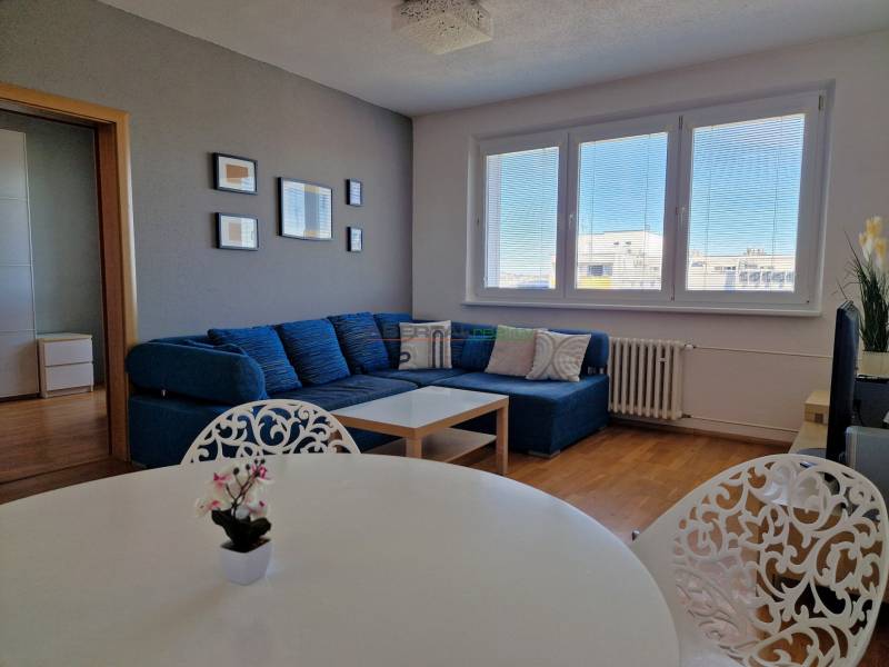 Wohnzimmer einer 3-Zimmer-Wohnung mit Sofa, weißem Tisch und Boden in Holzoptik.