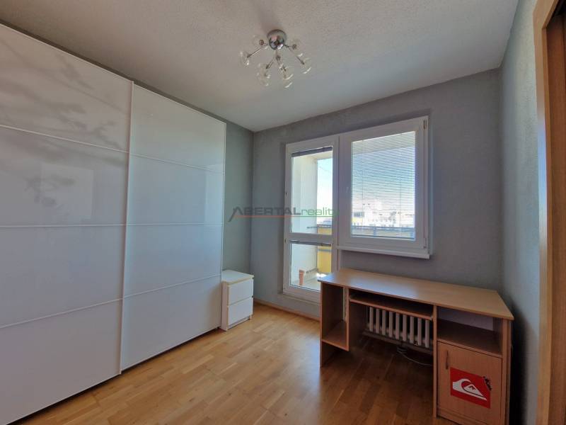 Ein Zimmer in einer 3-Zimmer-Wohnung mit einem Boden in Holzoptik, einem Tisch und einem Schrank.