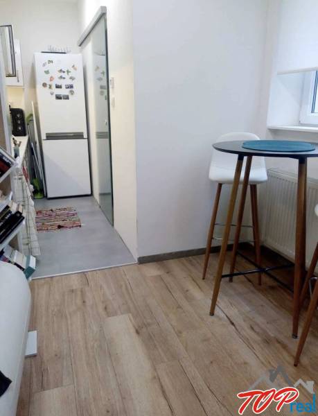 Küche in einer Einzimmerwohnung mit Holzboden, hoher Tisch und Stühle.