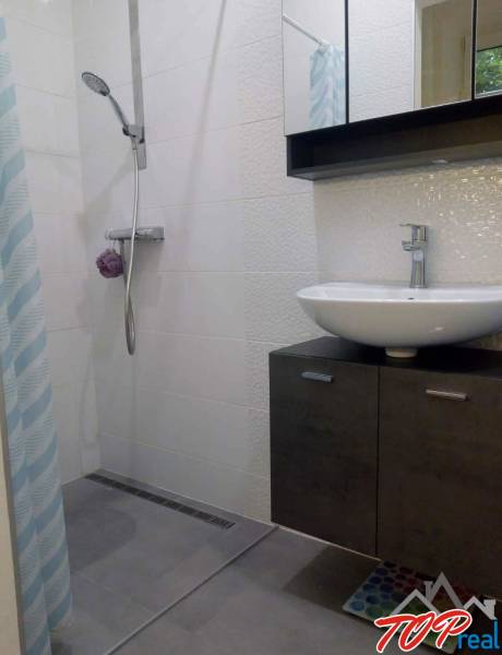 Badezimmer mit moderner Duschkabine in einer Einzimmerwohnung, helle Fliesen, Waschbecken.