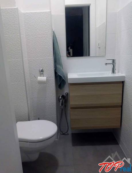 Kompaktes Badezimmer mit Waschbecken und Schrank in einer Einzimmerwohnung, Fliesen mit feiner Textur.