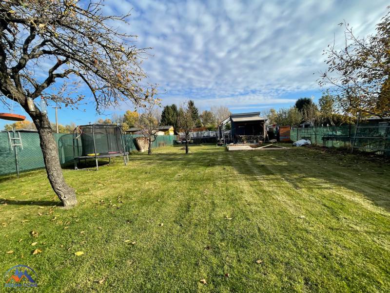 Ein Trampolin im Garten der Hütte in der Neuen Siedlung in Komárno mit einem Apfelbaum und blauem Himmel.
