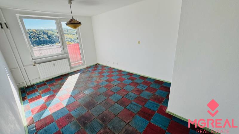 Ein Zimmer in einer Einzimmerwohnung mit farbigem Boden und großen Fenstern, Blick auf die Natur.