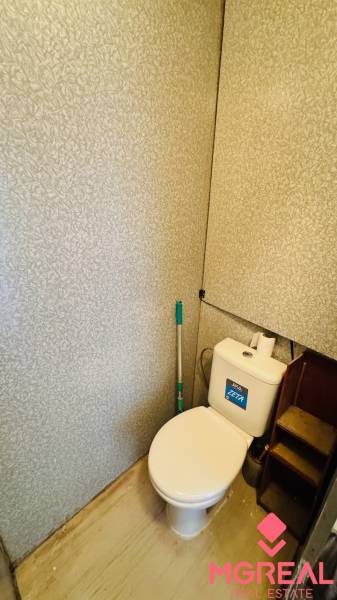 Toilette in einer Einzimmerwohnung mit Spülkasten und Wand mit Reliefmuster.