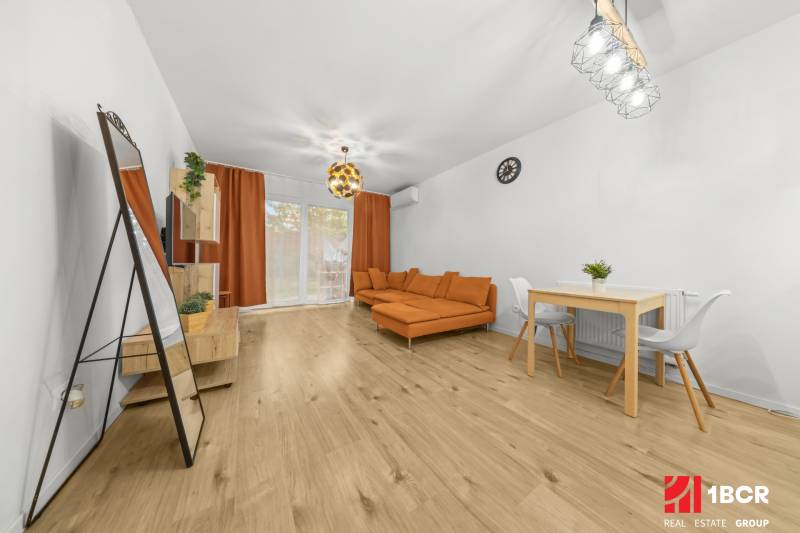 Wohnzimmer in einer Zweizimmerwohnung mit Holzboden, orangefarbenem Sofa und Esstisch.
