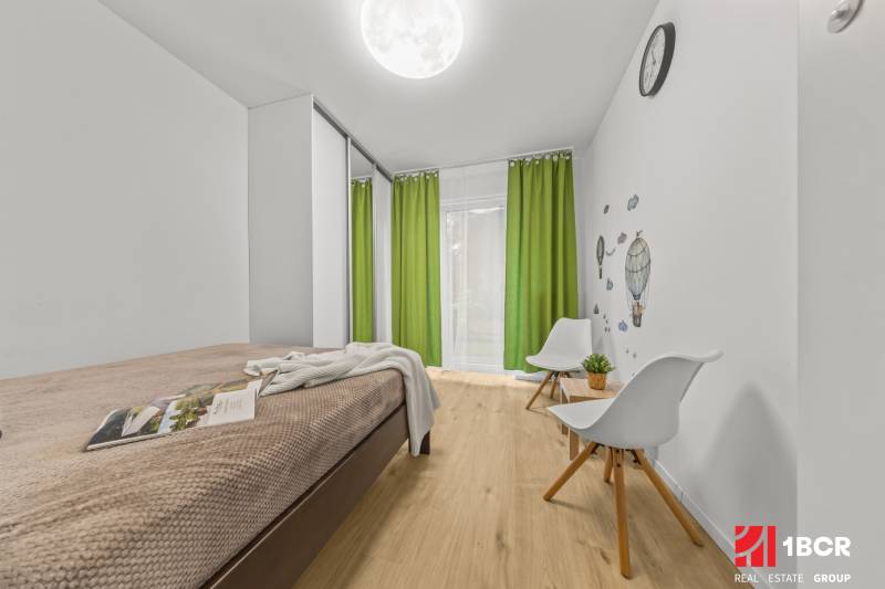 Helles Zimmer in einer 2-Zimmer-Wohnung mit Bett, grünen Vorhängen und Holzboden.