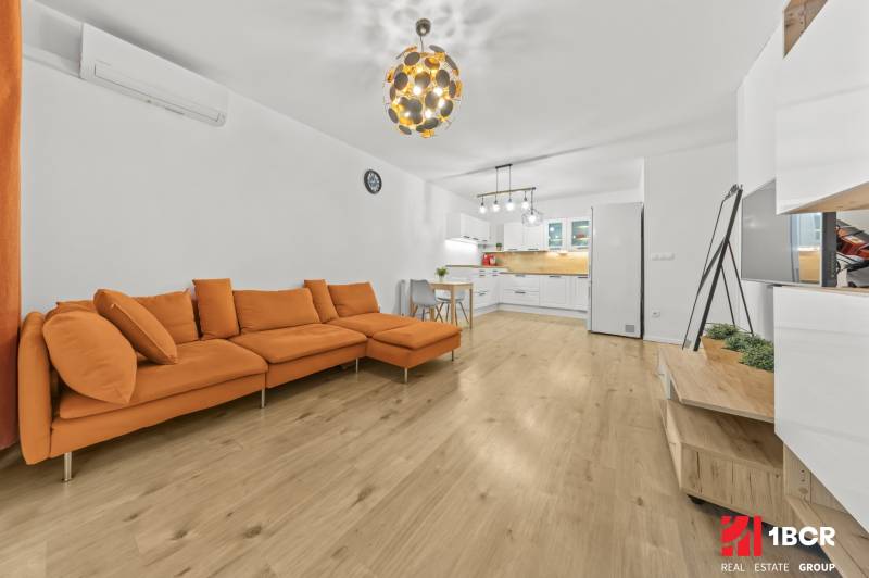 Wohnzimmer in einer 2-Zimmer-Wohnung mit einem orangefarbenen Sofa und einem Boden in Holzoptik.