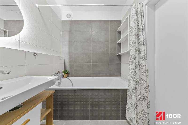Badezimmer in einer 2-Zimmer-Wohnung mit Badewanne, Waschbecken und Duschvorhang in neutralen Farben.