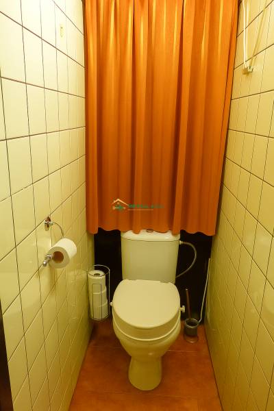 Toilette mit einem orangefarbenen Vorhang und hellen Fliesen in einer Zweizimmerwohnung.