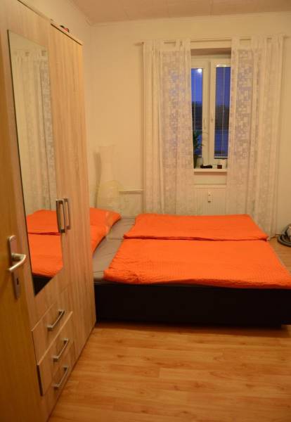 Schlafzimmer in einer 2-Zimmer-Wohnung mit orangefarbener Bettwäsche und Holzboden.