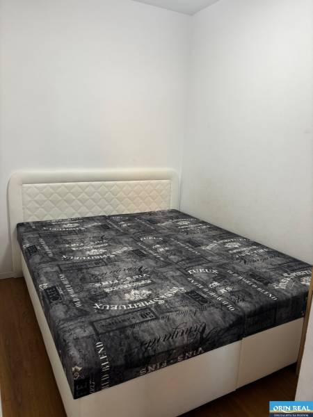 Schlafzimmer in einer 2-Zimmer-Wohnung mit Bett, hellen Wänden und Boden in Holzoptik.