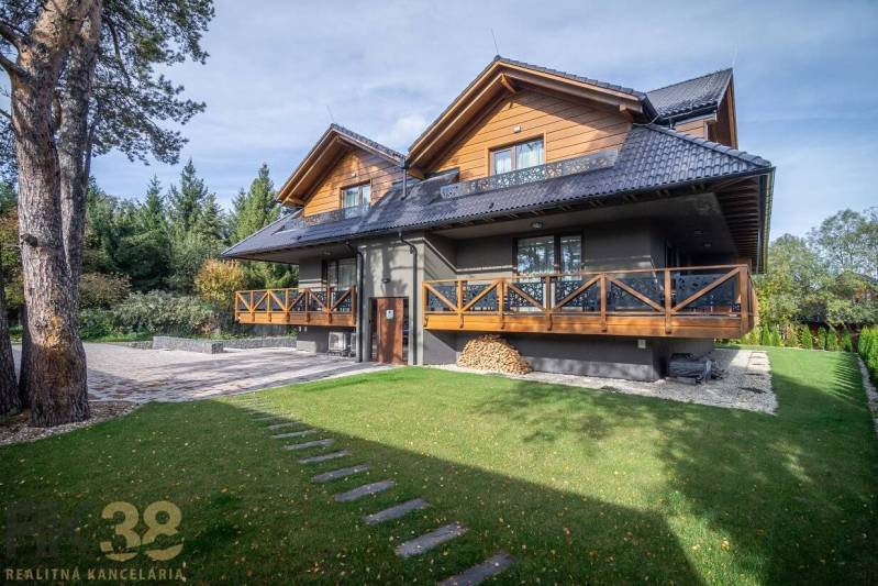Ein zweistöckiges Haus mit Holzelementen und einem grünen Rasen in Tatranská Lomnica.