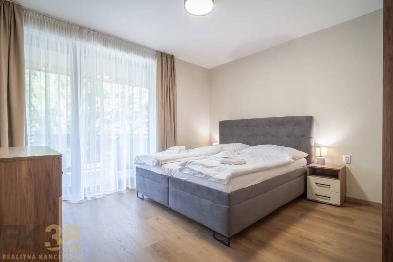 Schlafzimmer in einer 2-Zimmer-Wohnung mit hellen Vorhängen und einem Boden in Holzoptik.