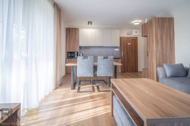 Innenraum einer 2-Zimmer-Wohnung mit Küchenzeile, grauen Stühlen und einem Boden in Holzoptik.