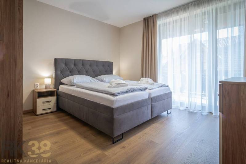 Schlafzimmer in einer 2-Zimmer-Wohnung mit einem großen Bett und einem Boden in Holzoptik.
