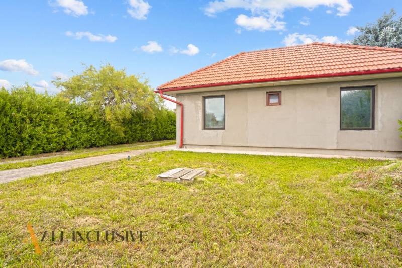 Ein Einfamilienhaus in Bátorove Kosihy mit einem roten Dach, umgeben von grünem Rasen und Sträuchern.