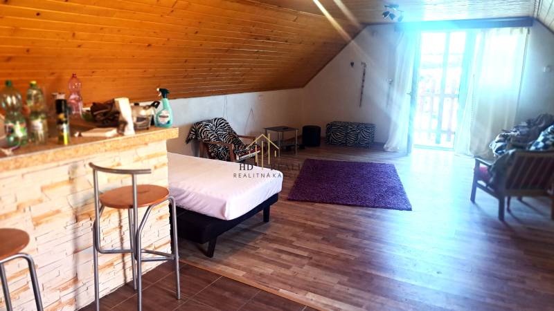 Innenraum einer Hütte mit Bartresen, Bett und Boden in Holzoptik.