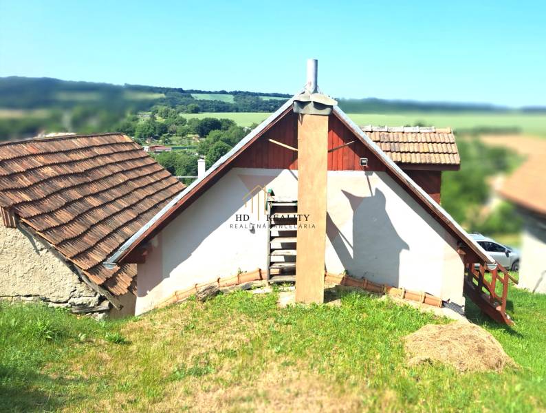 Ein Ferienhaus in Hontianske Trsťany mit traditionellem Schrägdach und einer Kulisse aus grüner Landschaft.