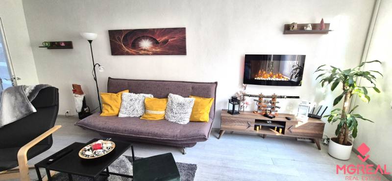 Wohnzimmer in einer Zweizimmerwohnung mit Sofa, Regal und Elektrokamin.