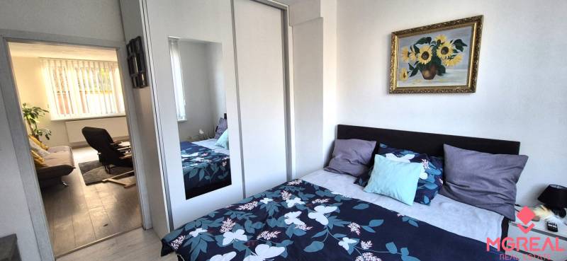 Schlafzimmer mit buntem Bett und Schrank in einer 2-Zimmer-Wohnung, führt ins Wohnzimmer.