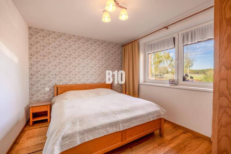 Ein Schlafzimmer in einem Einfamilienhaus mit einer geblümten Tapete und einem Boden in Holzoptik.