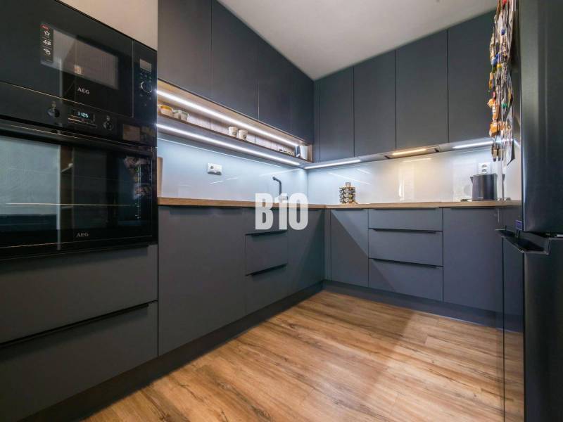 Küche in einer 3-Zimmer-Wohnung mit dunklen Schränken und einem Boden in Holzoptik.