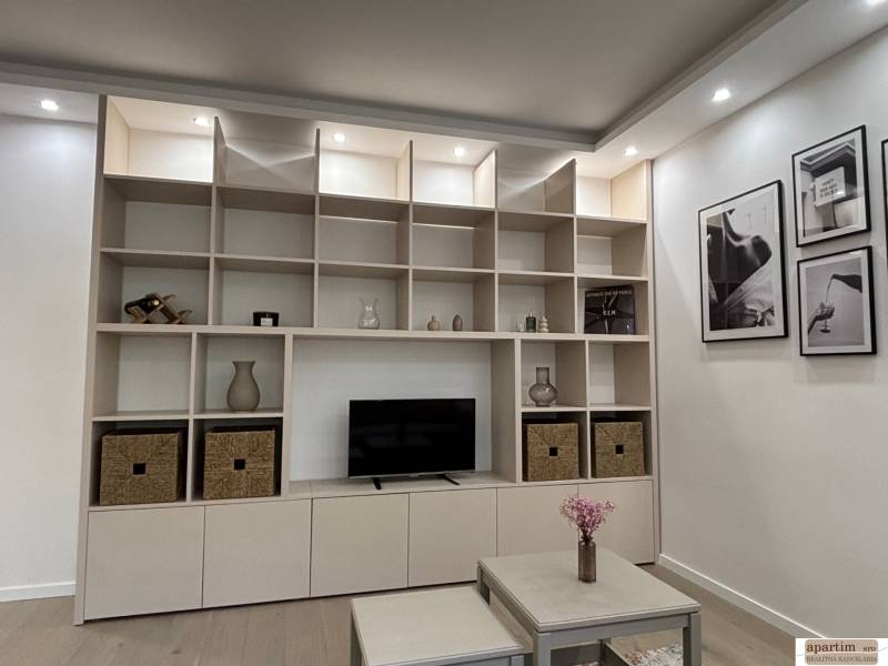 Ein Wandschrank mit Regalen und Dekorationen in einer Zweizimmerwohnung, daneben ein Tisch mit Blumen.