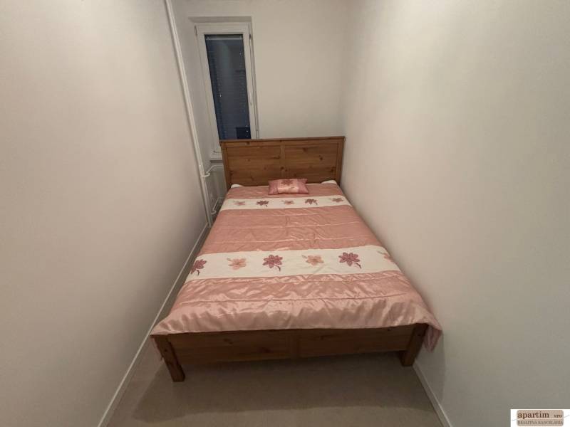 Schmales Schlafzimmer in einer 2-Zimmer-Wohnung mit einem Holzbett und einer Blumenbettdecke.