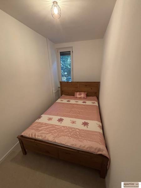Schmales Schlafzimmer mit einem Bett mit gemustertem rosa Überwurf in einer Zweizimmerwohnung.