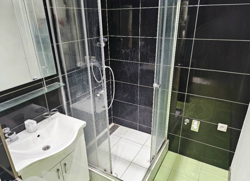 Badezimmer in einer 2-Zimmer-Wohnung mit Dusche und Waschbecken, schwarze Fliesen.