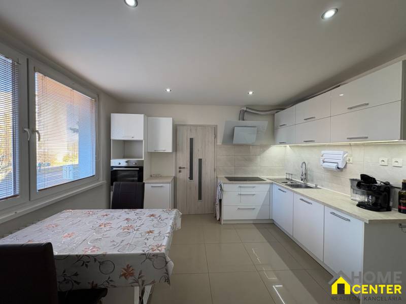 Küche in einer 3-Zimmer-Wohnung mit weißen Schränken und Fliesen, Boden mit Holzdekor.