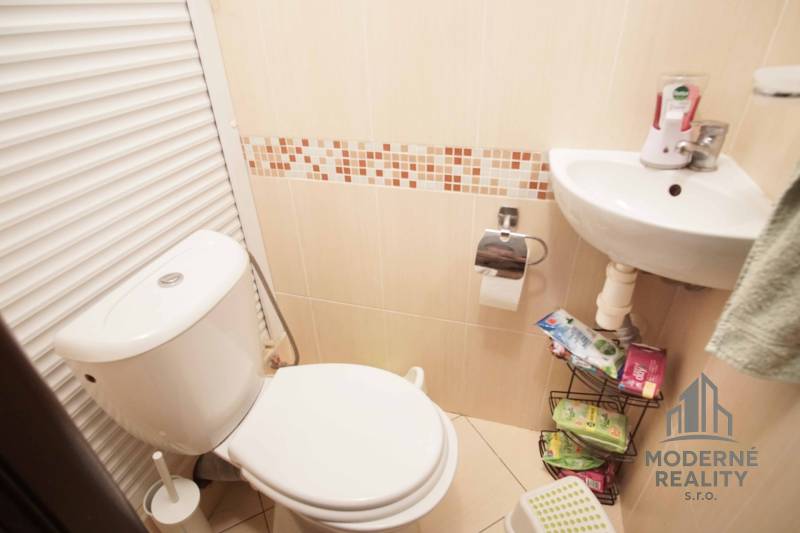 Badezimmer mit Toilette und Waschbecken in einer 3-Zimmer-Wohnung, beige Fliesen.