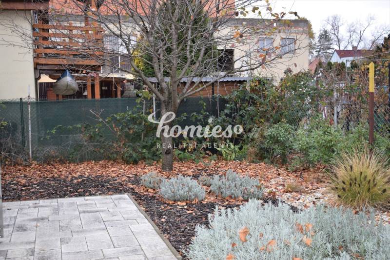 Garten bei einem Einfamilienhaus in Nitra, mit Bäumen, Stauden und gepflasterter Fläche.