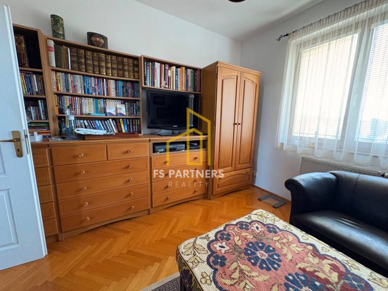 Ein Zimmer in einer Mehrzimmerwohnung mit Bibliothek, Fernseher und einem Boden in Holzoptik.