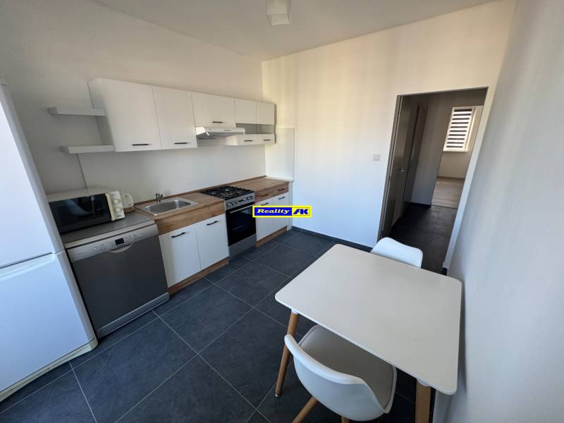 Küche in einer 3-Zimmer-Wohnung mit weißen Schränken und Tisch, auf dunklem Boden.