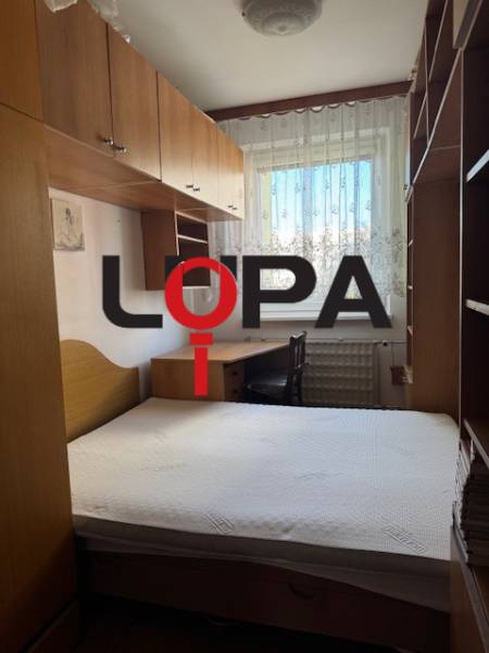 Schlafzimmer in einer 3-Zimmer-Wohnung mit Bett, Schränken und Fenster mit Spitzenvorhängen.