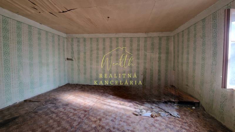 Ein Zimmer in einem Einfamilienhaus mit beschädigter Decke, Tapeten und einem Boden mit Holzdekor.