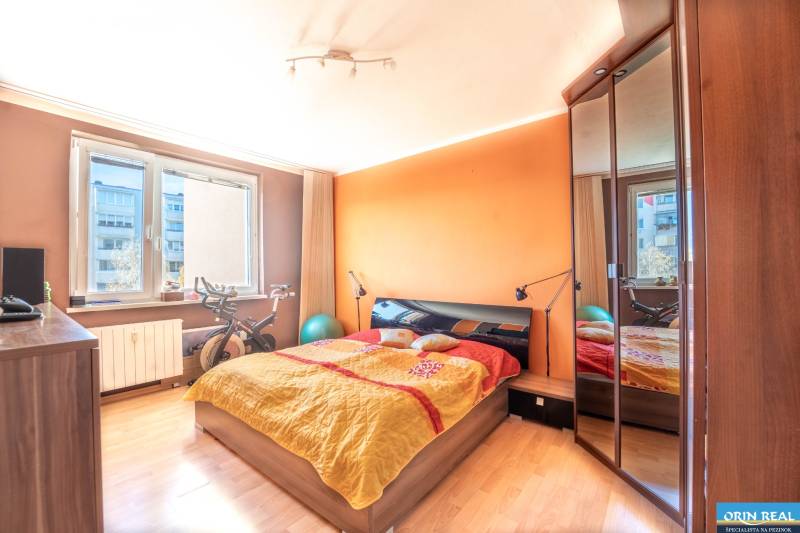 Schlafzimmer mit orangefarbener Wand, Bett und Boden mit Holzdekor in einer 3-Zimmer-Wohnung.