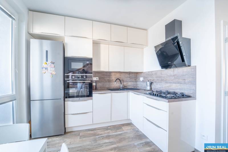 Küche in einer 3-Zimmer-Wohnung mit weißen Möbeln, eingebauten Geräten und einem Boden in Holzoptik.