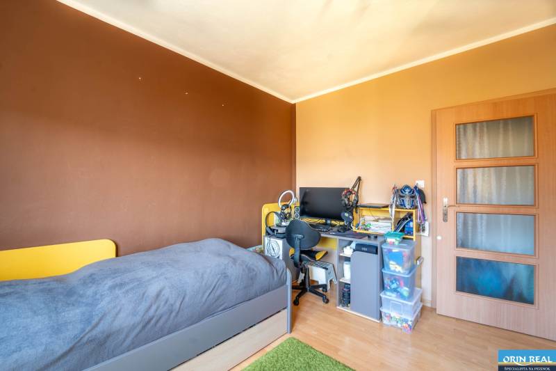 Ein Zimmer in einer 3-Zimmer-Wohnung mit einem Bett, einem Schreibtisch und einem Boden in Holzoptik.