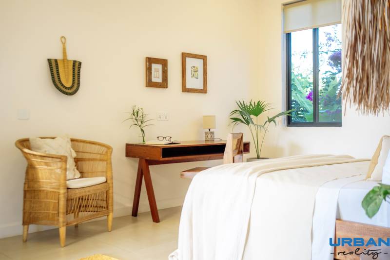 Helles Schlafzimmer in einem Einfamilienhaus mit einem Rattansessel und einem Holztisch.