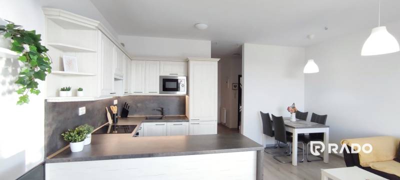 Die Küche einer 2-Zimmer-Wohnung mit weißen Schränken und einem Esstisch, der Boden hat eine Holzoptik.