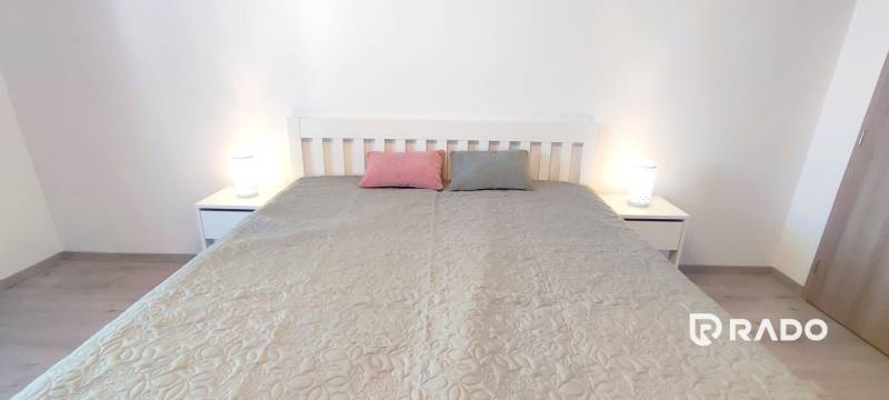 Schlafzimmer mit Bett, zwei Kissen und Nachttischen in einer Zweizimmerwohnung.