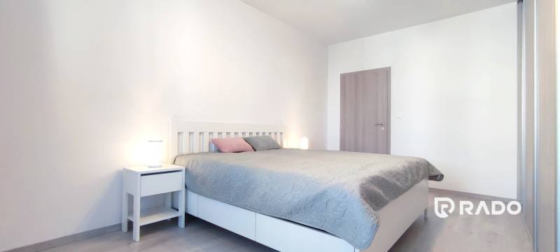 Schlafzimmer mit Bett, Nachttisch und Boden mit Holzdekor in einer 2-Zimmer-Wohnung.