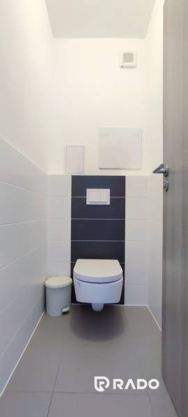 Toilette mit weißen Fliesen und hängender Toilettenschüssel in einer 2-Zimmer-Wohnung.