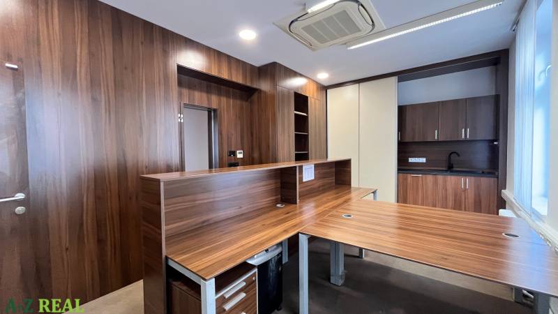 Ein Büro mit einem Boden in Holzoptik und einer Kochnische, breiter Holztheke.